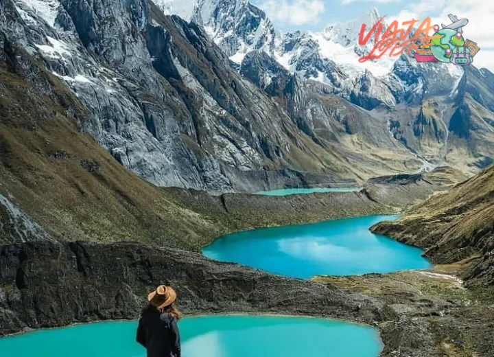 <p>Montañas nevadas de la Cordillera Blanca reflejadas en una laguna turquesa, con un sendero rocoso bordeando el paisaje.…
